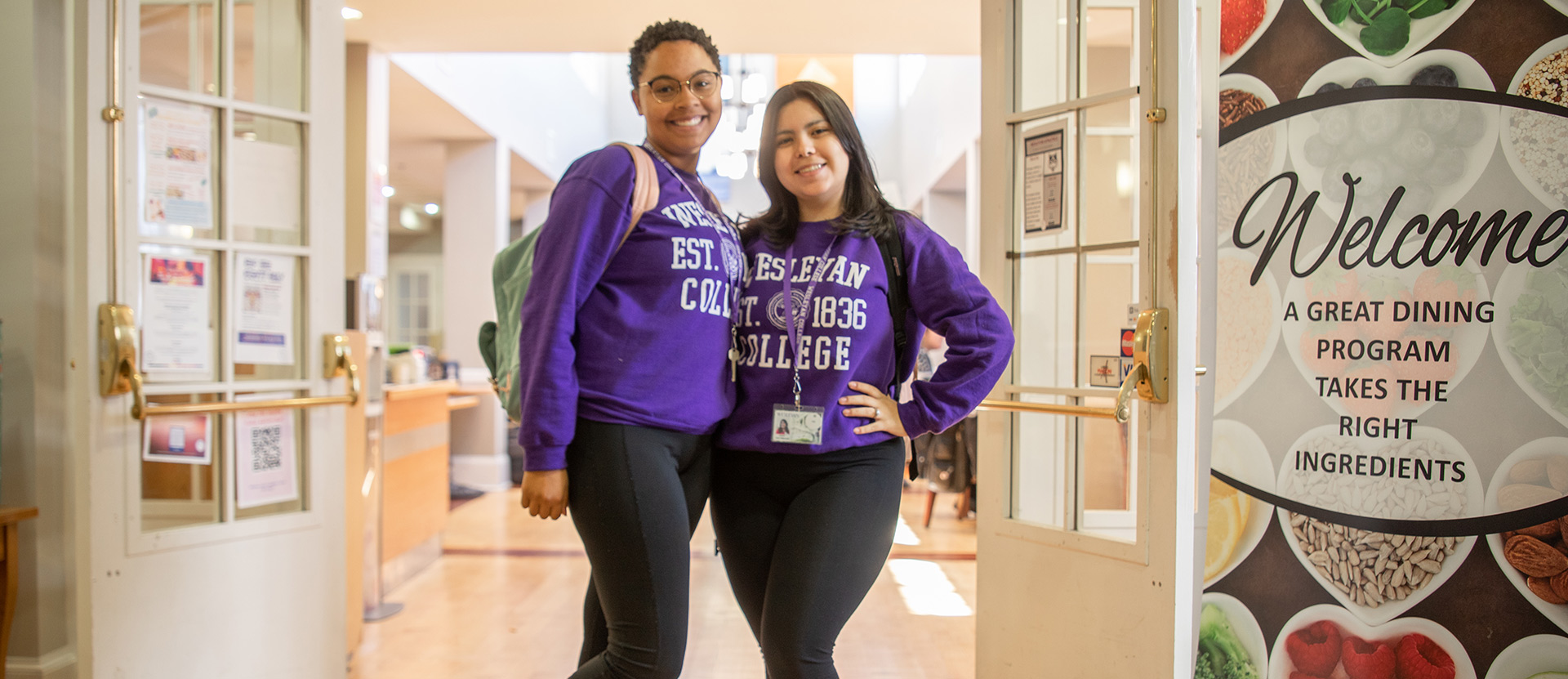 Two students wearing purple wesleyan sweatshirts hugging