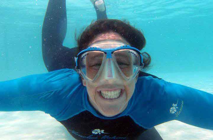 Janelle Fleming swimming in the ocean with googles and looking into the camera.