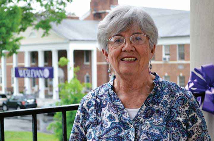 Alumnae Julia Ketcham on outside porch of Candler with Olive Swann Building behind her.