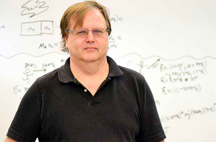 Faculty member Charles Benesh stands in front of white board