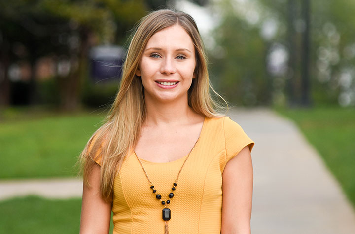 Faculty member Holly Cole stands outside in the quad and smiles for the camera.