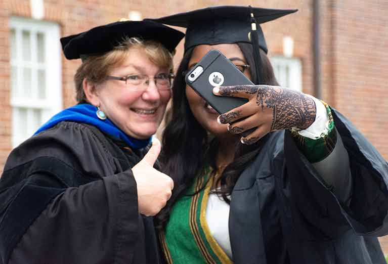 Professor and student take selfie while dressed in regalia.
