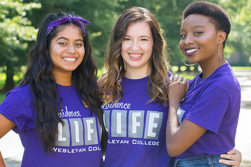 Three students hugging and smiling outside.