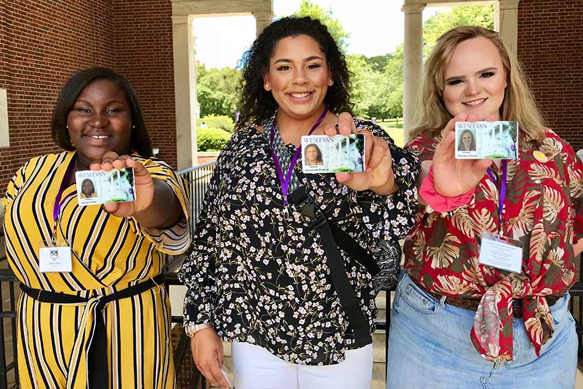 Three students hold up their new student id badges