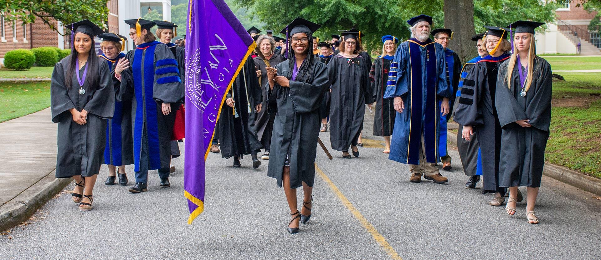 Students in regalia march with the Wesleyan Flag