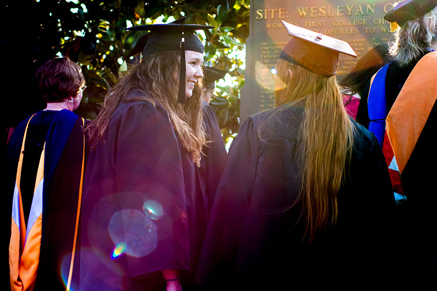 Two Wesleyan graduates in gowns outside.