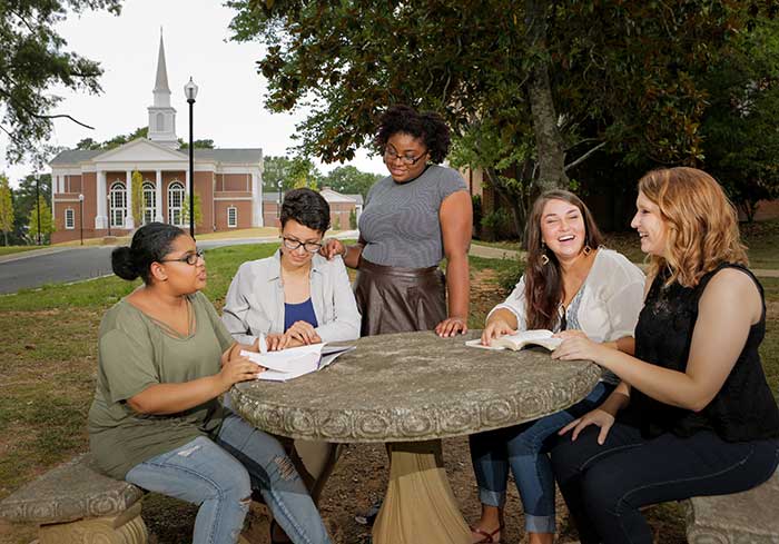 Students sit outside a table with the Pierce Chapel behind them