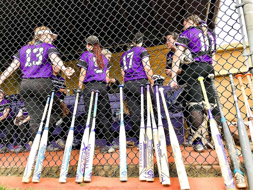 Softball dugout with bats and players.