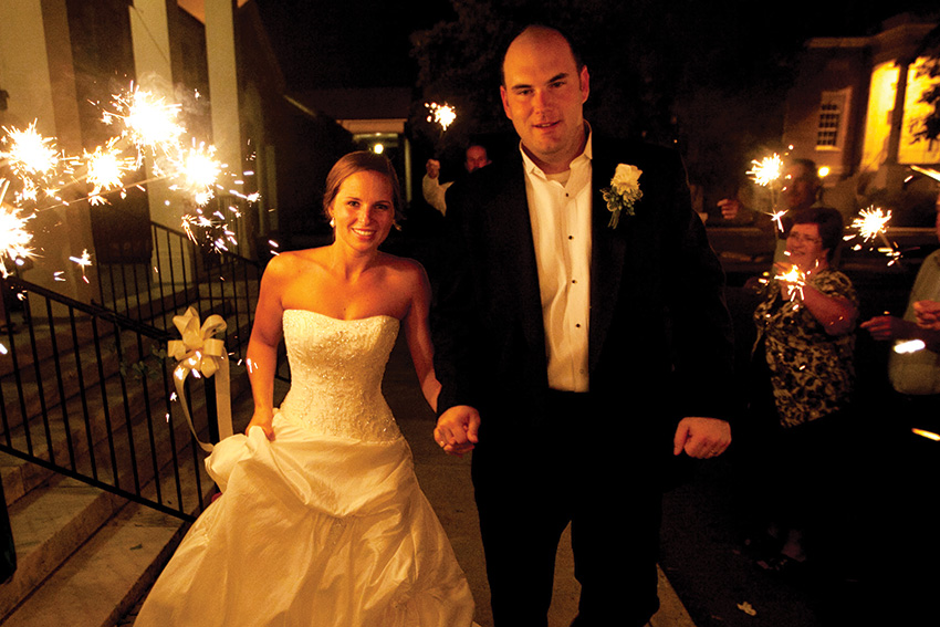 Bride and Groom walk to car at night with sparklers in the background